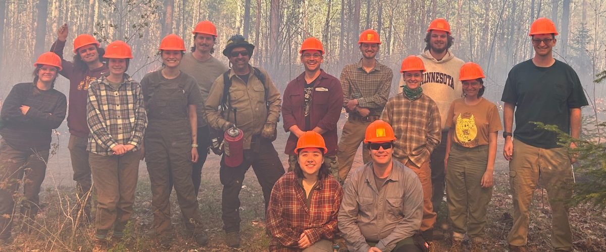 Students in orange hardhats standing in a smoky forest