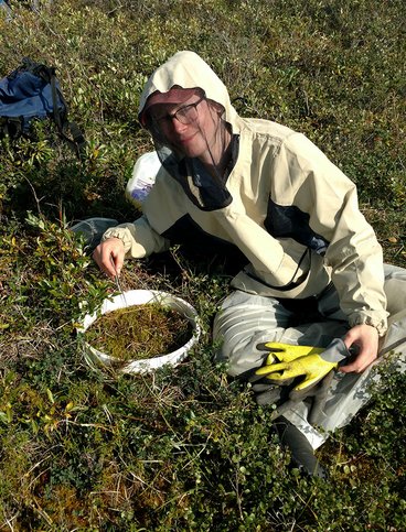 Tyler Baumann wearing a tyvek suit sitting next to a soil ring performing an earthworm extraction