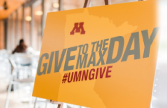 A yellow sign reads " Give to the Max Day #UMNGIVE".