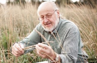 Don sits in a field an looks at a stalk of grain.