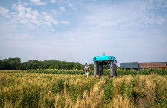 A person and a rover in a field on the St. Paul campus of the University of Minnesota