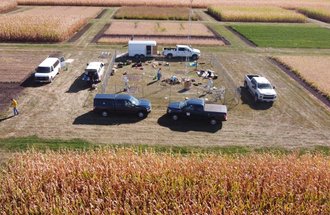 A drone image of trucks parked around a weather station enclosure. Equipment is spread across the ground and MDA staff work to install the new weather station.